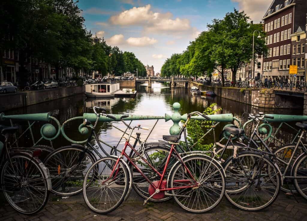 assorted color bicycles parked next to pastel green metal rails next to river in Amsterdam Netherlands